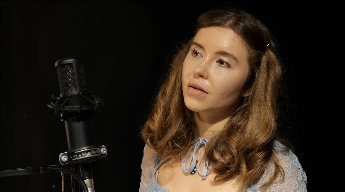 India Falconer singing at a studio microphone against a dark background